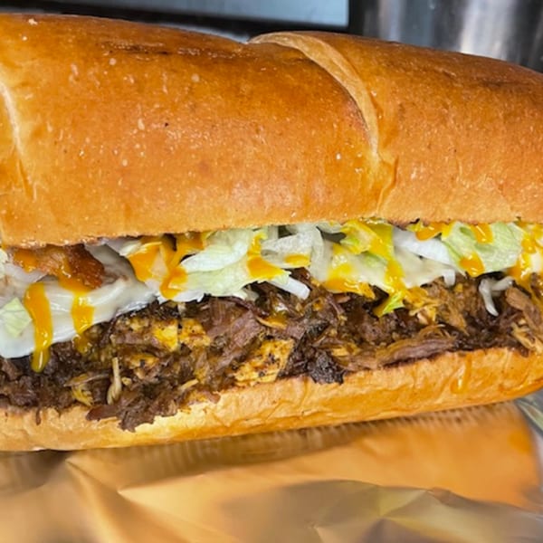 A FATBOYSBBQ pulled pork sub with shredded lettuce, white sauce, and mustard drizzle.
