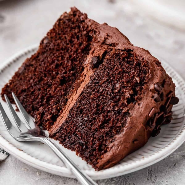 Two slices of rich chocolate cake with chocolate frosting and sprinkles on a white plate with a fork.