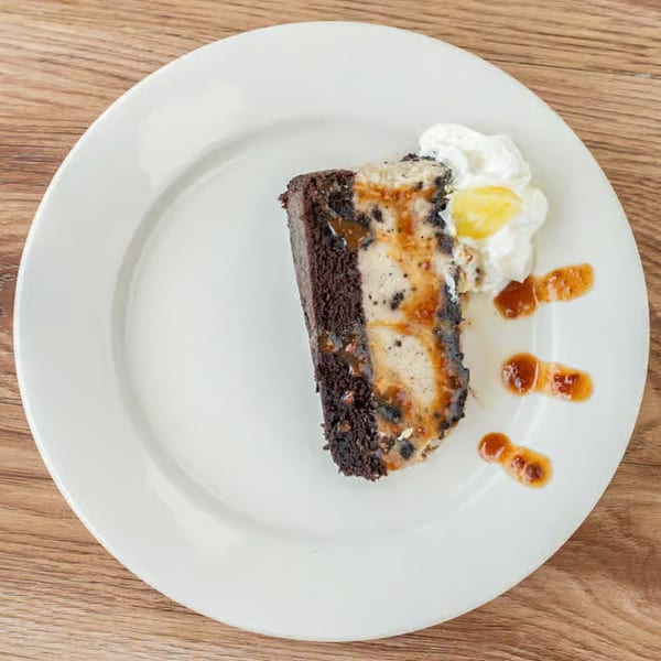 A slice of chocolate cake with creamy filling, whipped cream, and caramel drizzle on a white plate.