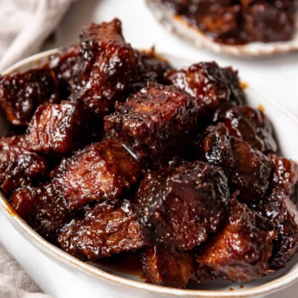 Close-up of FATBOYSBBQ's burnt ends, glistening with rich, dark barbecue sauce in a white bowl.