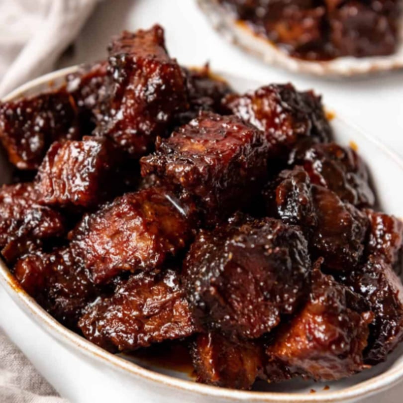 Close-up of FATBOYSBBQ's burnt ends, glistening with rich, dark barbecue sauce in a white bowl.