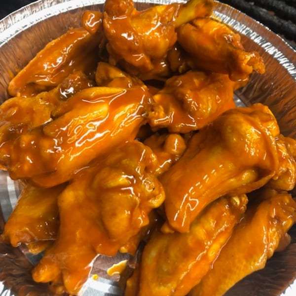 A close-up of FATBOYSBBQ's saucy orange chicken wings in a foil container.
